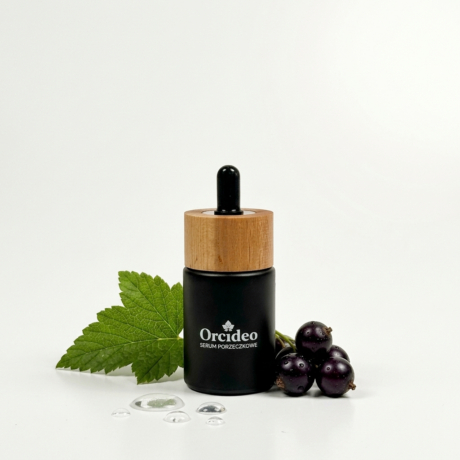 Buteleczka serum porzeczkowego Orcideo w otoczeniu owoców porzeczki i liścia.